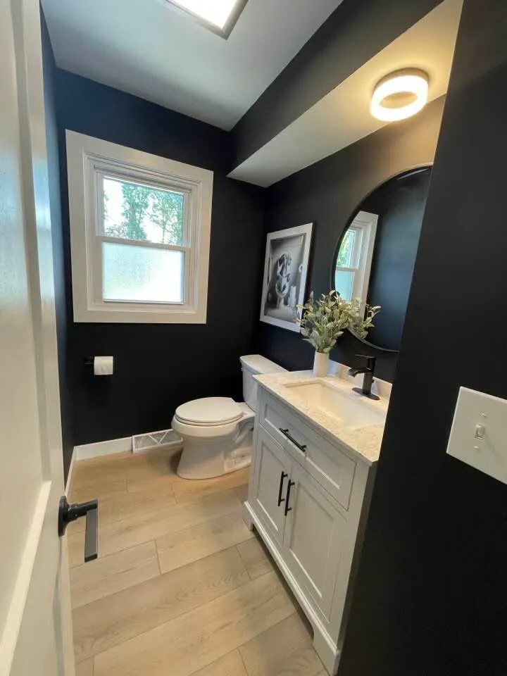 A powder bath with black walls, an arched mirror, a white vanity, and a window letting in daylight